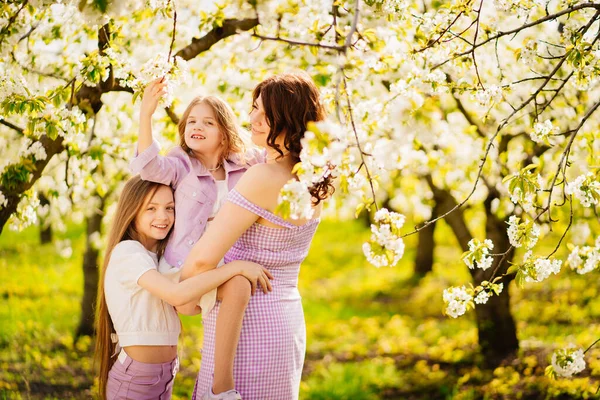 Счастливая мама и две дочери в цветущем весеннем саду. родительская любовь. — стоковое фото