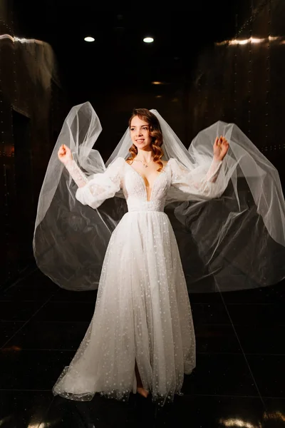 beautiful bride in a white elegant dress, with a veil goes down a dark corridor
