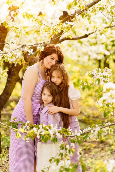 Счастливая мама и две дочери в цветущем весеннем саду. родительская любовь. — стоковое фото