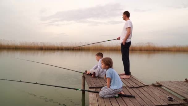 Vater und Sohn und Tochter auf einer Holzbrücke fangen Fische aus dem Fluss. — Stockvideo