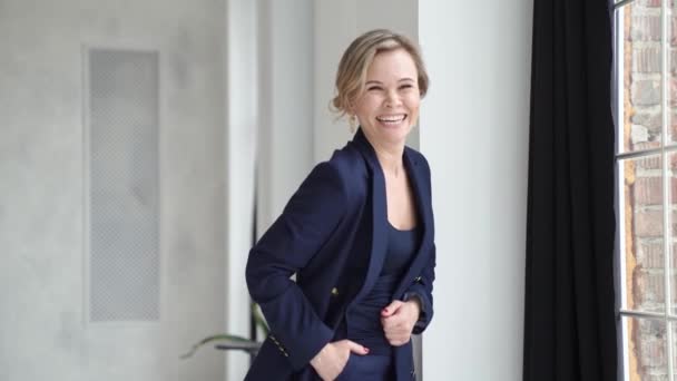 Una hermosa mujer con un traje azul posa junto a una ventana en un estudio fotográfico. — Vídeo de stock