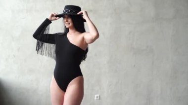 Gri duvarda siyah takım elbiseli ve şapkalı seksi kadın. sahne arkası fotoğraf çekimi