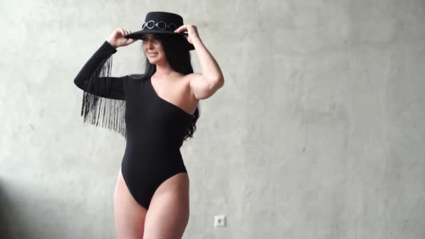 Szexi nő fekete öltönyben és kalapban a szürke falnál. színfalak mögött fotózás — Stock videók