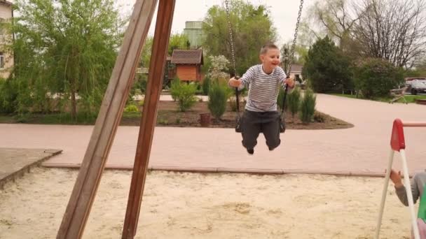 Junge schaukeln auf der Schaukel. Unterhaltung auf dem Kinderspielplatz. — Stockvideo