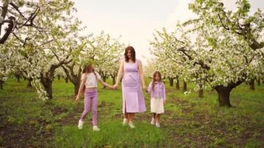 Anne, iki kızıyla birlikte bahçede, çiçek açan ağaçların arasında yürüyor..