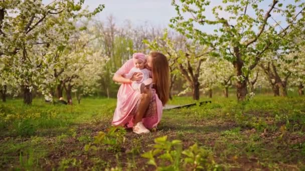 母と赤ん坊の娘は開花庭に座っています。赤ちゃんに残されたクリップ. — ストック動画