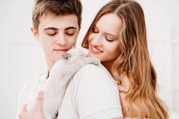 Um belo casal de jovens amantes segurando um pequeno gatinho branco. — Fotografia de Stock