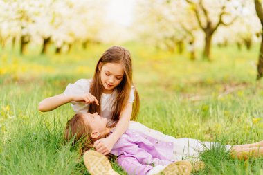 Bahçedeki çimenlikte çiçek açan iki uzun saçlı kız kardeş..