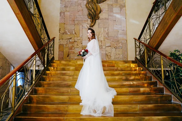 Portrait d'une mariée avec de longues boucles, dans une robe élégante sur l'escalier doré — Photo