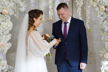 Nikah yüzüklerinizi takın. Gelin ve damat düğün töreninde bir çiçek kemerinde.