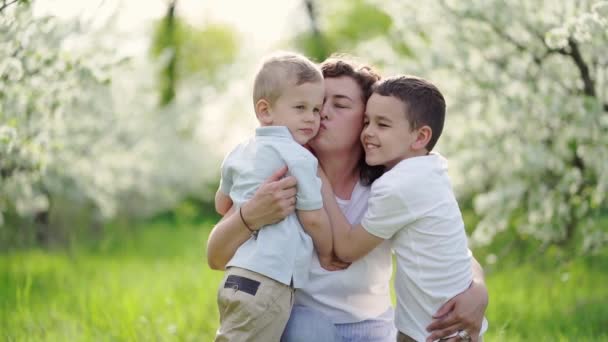 Madre con hijos besándose y abrazándose en el jardín floreciente. día de las madres — Vídeos de Stock