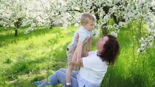 Мама грається в весняному саду з малим сином, кидає дитину.. — стокове відео