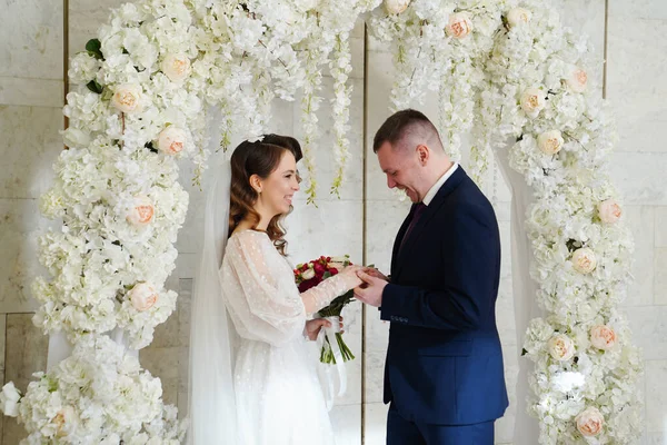 Troca de casamento rings.bride e noivo em um arco de flores na cerimônia de casamento — Fotografia de Stock