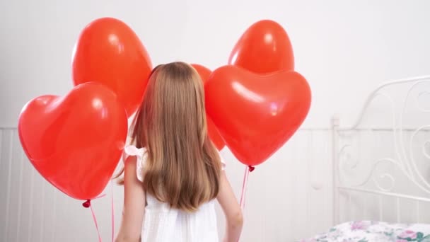 Vista trasera. chica se gira con globos rojos en forma de corazones en la cama — Vídeos de Stock