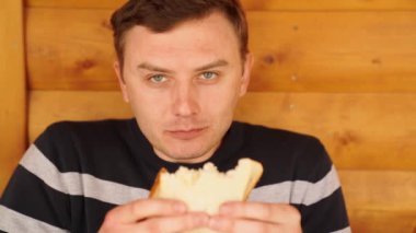 Bir adam beyaz ekmekten yapılmış bir sandviçi ısırır ve yer.. 