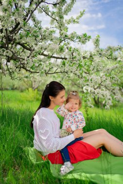 Anne ve kızı parkta çimenlikte çiçek açan bir ağacın yanında pikniğe gitmişler.. 