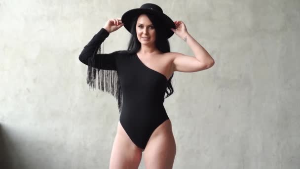 Kvinna i body suit och hatt vid grå vägg. fotografen korrigerar frisyr av modell — Stockvideo