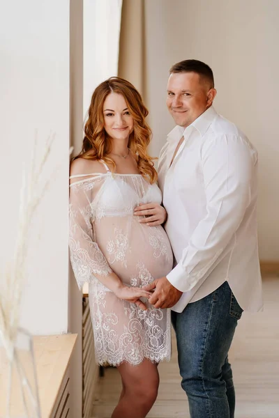 a man and a woman in white waiting for the birth of a child against the wall