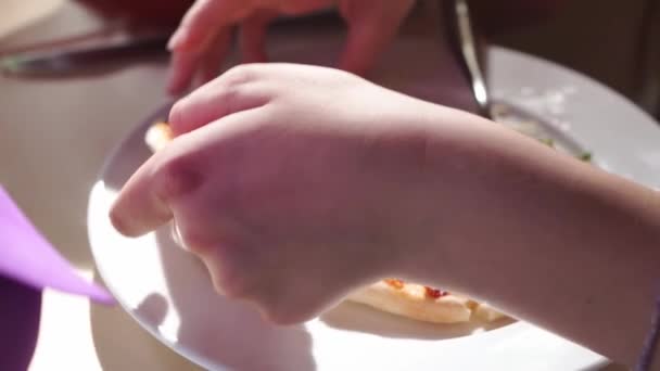Klein meisje pakt een stuk pizza en bijt af.. — Stockvideo