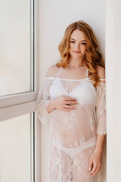 Hermosa mujer embarazada en vestido de encaje junto a la ventana. belleza del cuerpo femenino. — Foto de Stock