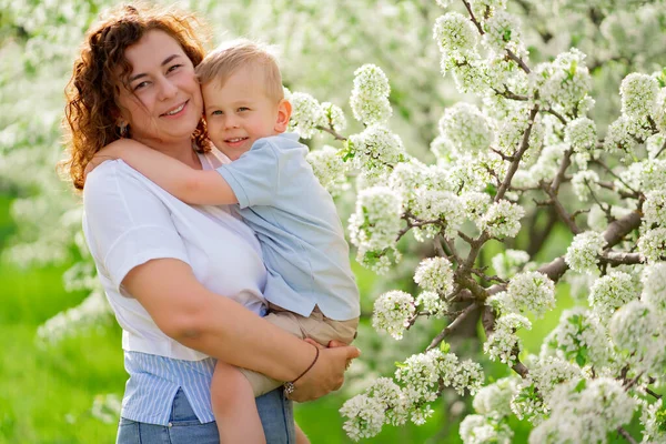 Мать держит своего маленького сына в цветущем весеннем саду. родительская любовь и забота — стоковое фото