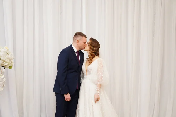 Hermosa y feliz novia y novio contra el fondo de la cortina blanca —  Fotos de Stock