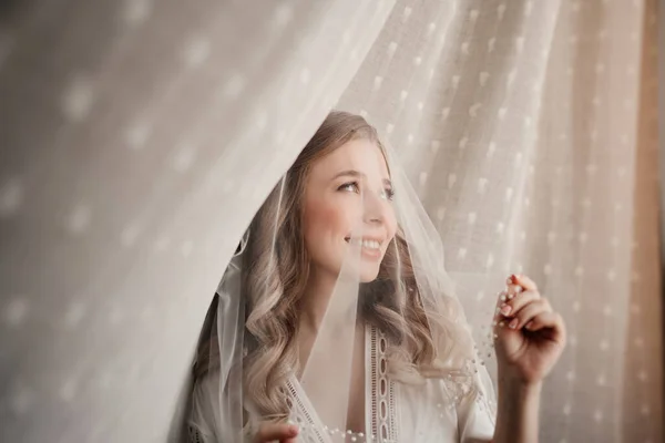 花嫁の優しい朝だ。白いカーテンの下にベールの中の美しい若い女性 — ストック写真