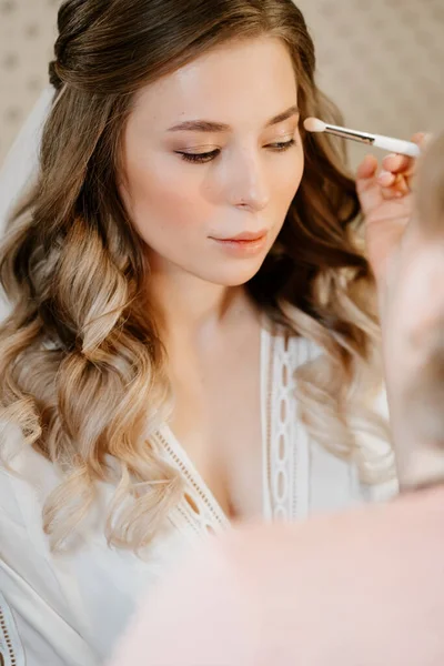 A beautiful girl with long hair do eye makeup. — Stock Photo, Image