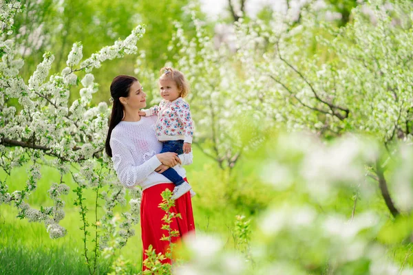 Mamá en un paseo con una hija en sus brazos en el parque con árboles florecientes. — Foto de Stock