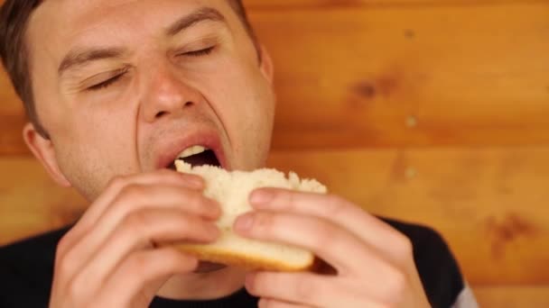 Een man bijt en eet een broodje van wit brood. — Stockvideo