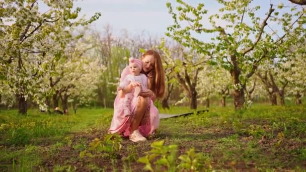 母は靴ひもの赤ん坊を結び、開花庭に座る。赤ちゃんに残されたクリップ. — ストック動画