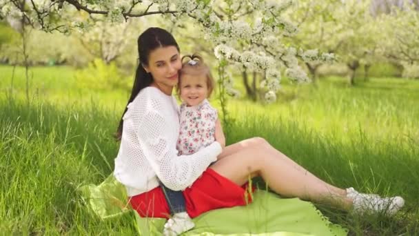 Mutter mit Tochter bei einem Picknick auf dem Rasen im Park an einem blühenden Baum. — Stockvideo