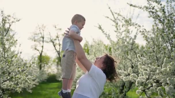 Mamma leker i vårträdgården med en ung son, virvlar och kastar upp barnet. — Stockvideo