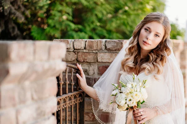 Belle mariée avec un bouquet de fleurs à la clôture. — Photo