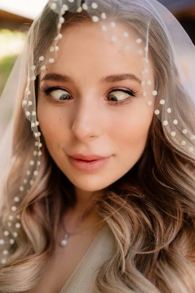 funny bride with long wavy hair under the veil outside. Wedding make-up.