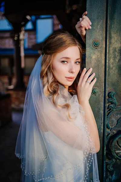 Novia suave en vestido blanco está de pie por hermosas puertas de metal negro en estilo retro — Foto de Stock