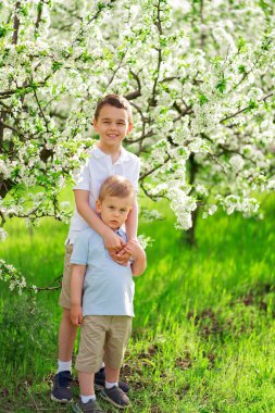 Çiçek açan ağaçların arasında çimenlikte iki küçük çocuk. Kırsal kesimde hayat. 
