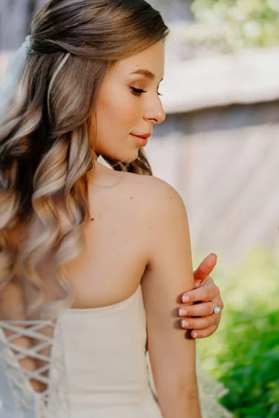 Vista trasera. novia con el pelo ondulado largo en el jardín. Maquillaje de boda. — Foto de Stock
