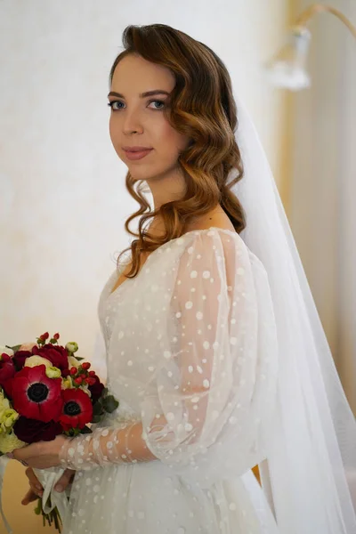 Schöne Braut mit langen Locken, in einem eleganten Kleid mit einem Strauß — Stockfoto