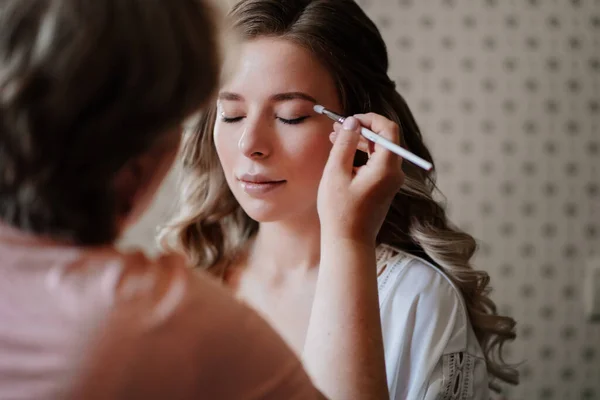 A beautiful girl with long hair do eye makeup. — Stock Photo, Image