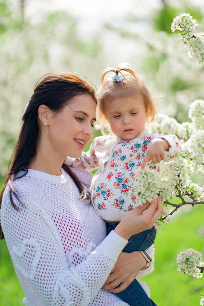 Мама с маленькой дочкой в руках в парке у цветущих деревьев. — стоковое фото