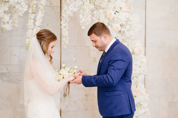 Schöne und glückliche Brautpaare tauschen Ringe in einem Blumenbogen aus — Stockfoto