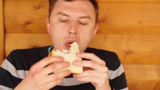 Un hombre muerde y come un sándwich hecho de pan blanco. — Vídeos de Stock