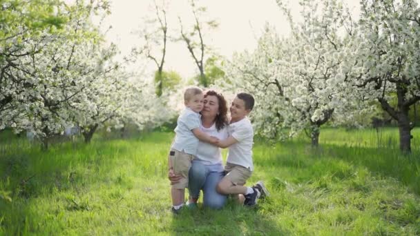 Mama cu fii sarutandu-se si imbratisandu-se in gradina cu flori. ziua mamei — Videoclip de stoc