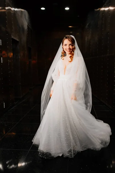 Noiva bonita em um vestido elegante branco, com um véu desce um corredor escuro — Fotografia de Stock