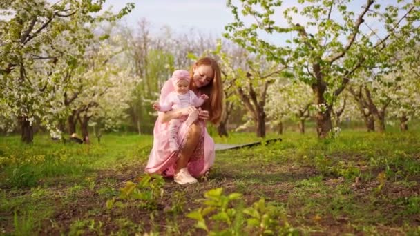 Anya cipőfűzőt köt, bébi, ülj a virágos kertben. ajakhasadék csecsemőknél. — Stock videók