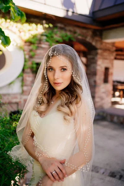 Braut mit langen welligen Haaren unter dem Schleier im Garten. Hochzeits-Make-up. — Stockfoto