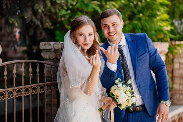 La novia y el novio muestran anillos de boda de pie junto a la valla retro — Foto de Stock