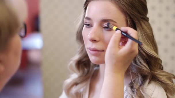 Ein schönes Mädchen mit langen Haaren machen Augen Make-up mit einem Pinsel. — Stockvideo