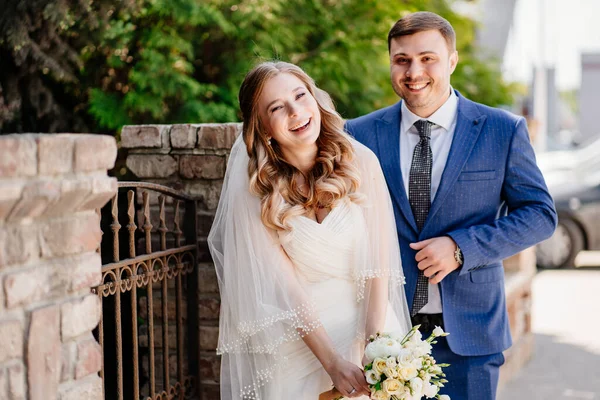 La novia y el novio felices de pie junto a la valla retro — Foto de Stock